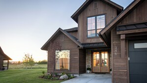 Une maison moderne à deux étages, dotée d’une façade en pierre, de grandes fenêtres et d’une pelouse bien entretenue.