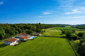Ländliche Landschaft mit Häusern, einem Schwimmbad und grünen Feldern.