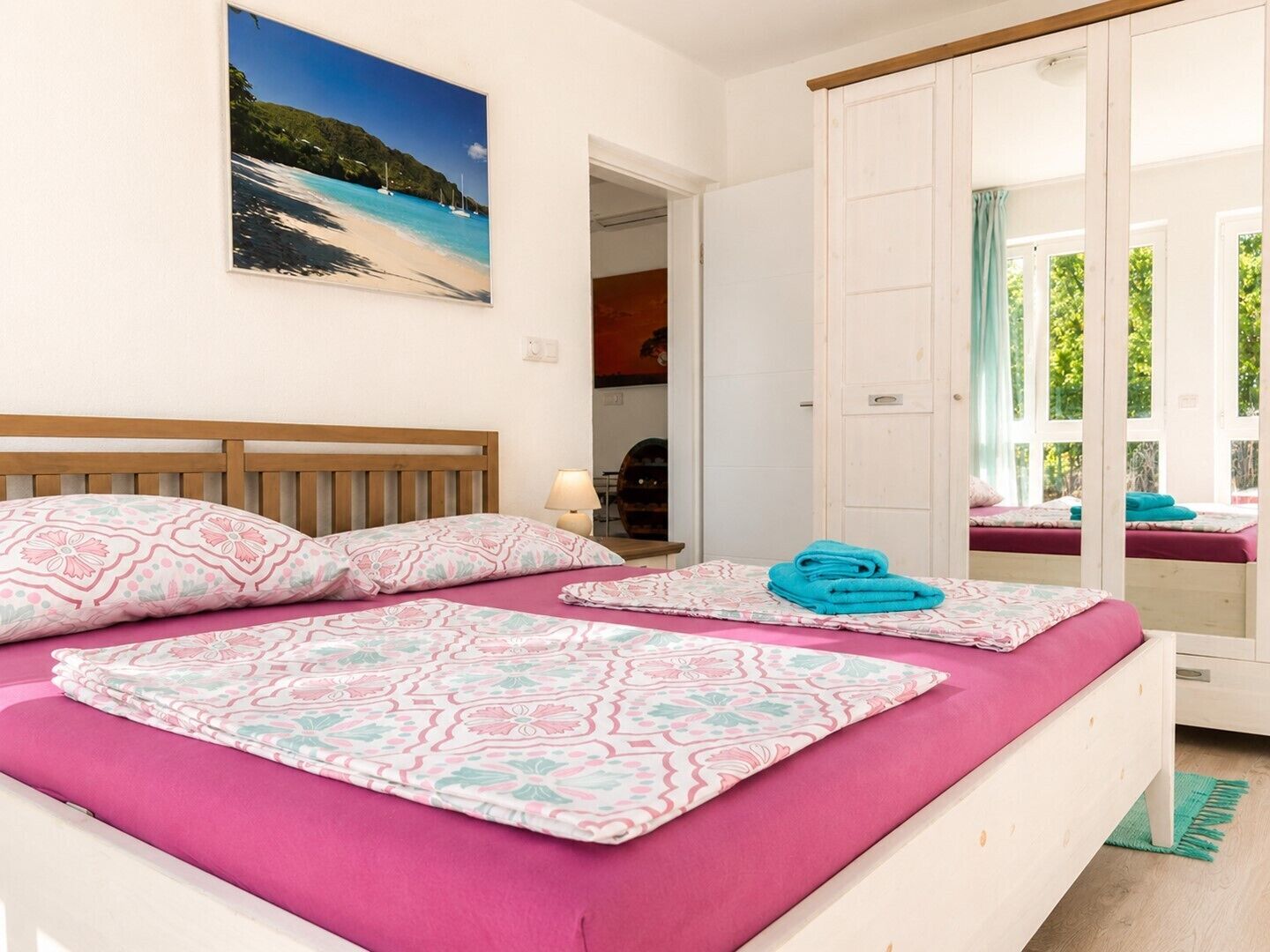 A bedroom with a bed, a painting of a beach, and a door leading to a balcony.
