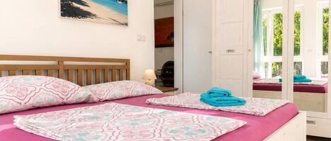 A bedroom with a bed, a painting of a beach, and a door leading to a balcony.