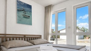 Un dormitorio con una cama grande, vista a la playa y un cuadro de un barco en el agua.