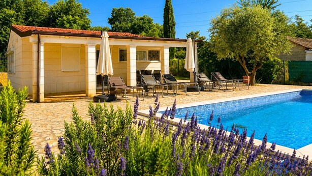 Un área junto a la piscina con sillones de descanso, un espacio de estar cubierto y una piscina.