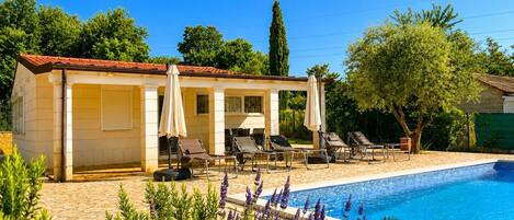 Un espace aménagé au bord de la piscine, avec des chaises longues, un coin salon couvert et une piscine.
