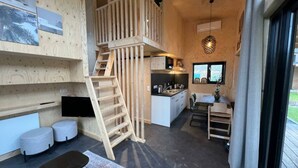 Un interior de madera compacto con cocina, comedor y un dormitorio en entrepiso accesible por una escalera de madera.