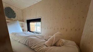 Una cama individual con ropa de cama blanca, una ventana con persianas y una pared de madera con un adorno de hoja.
