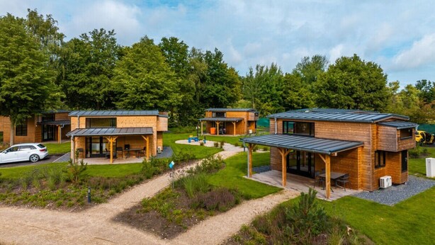 Una hilera de cabañas modernas con mobiliario exterior, rodeadas de exuberante vegetación y un cielo despejado.