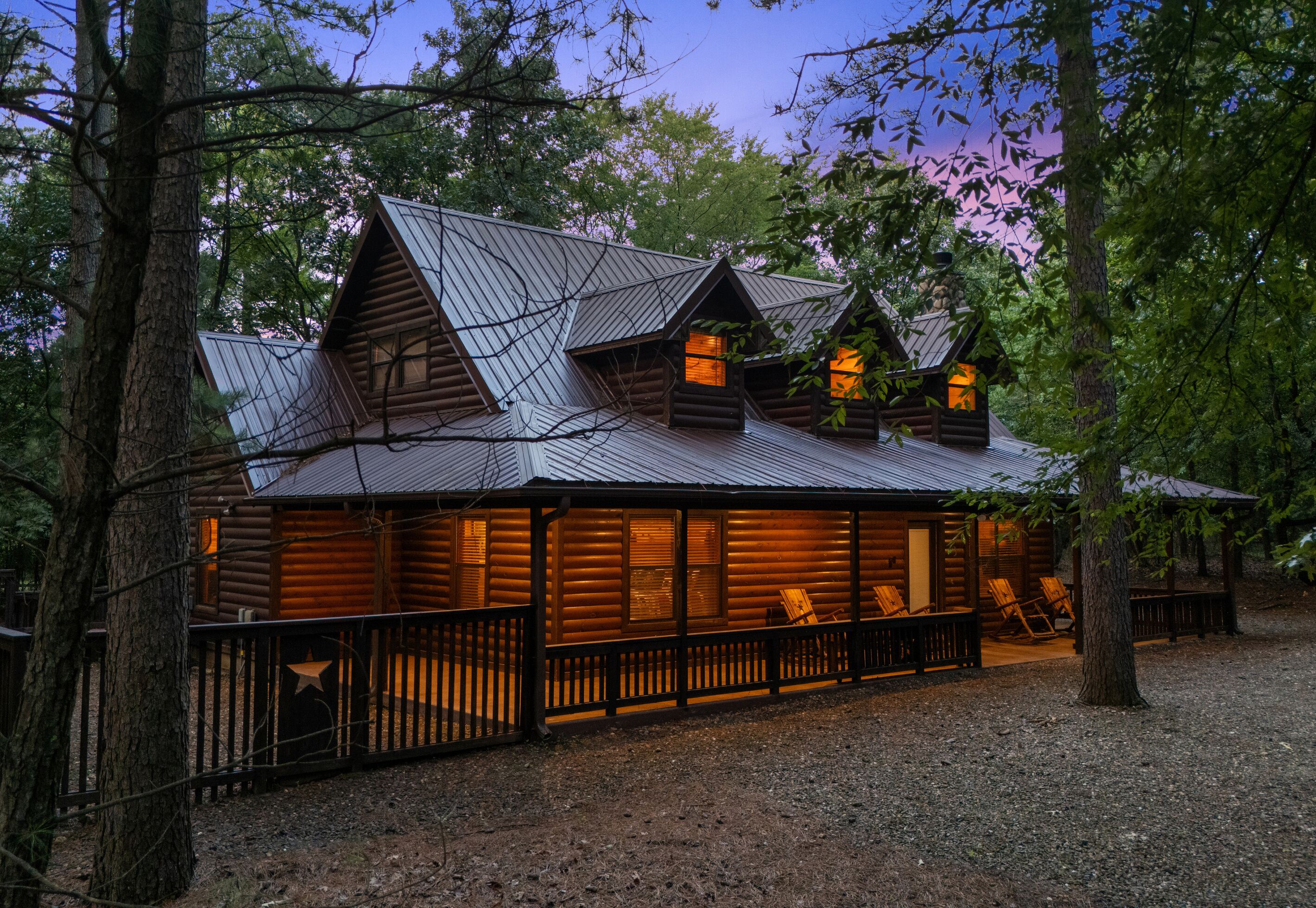 A log cabin with a metal roof, wooden deck, and a fenced area.