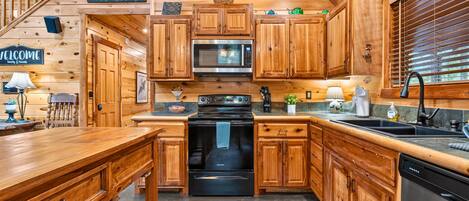Interior de una cabaña de madera con cocina, que incluye un microondas, estufa y lavaplatos.