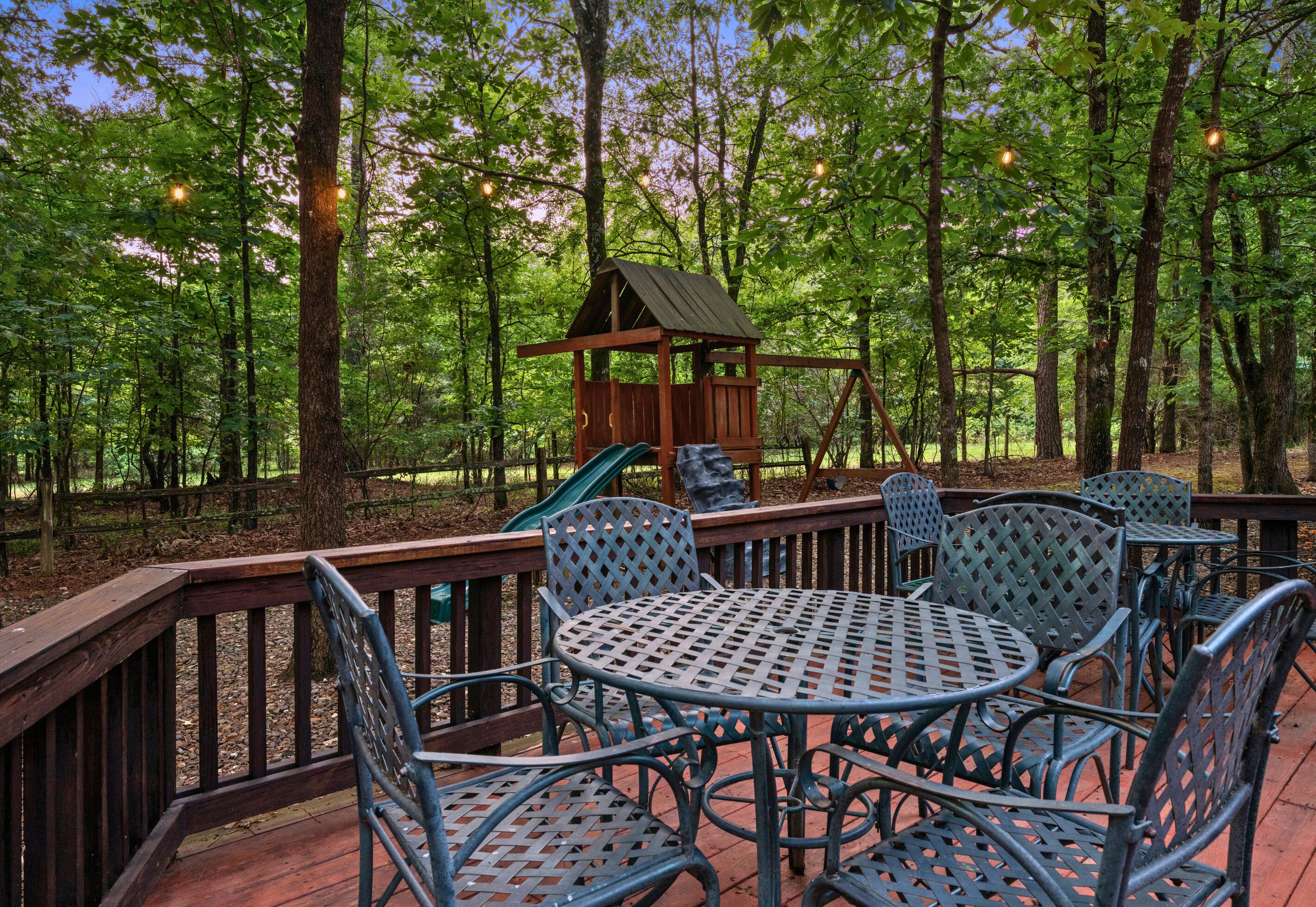 A wooden deck with metal chairs and tables, surrounded by a forest.
