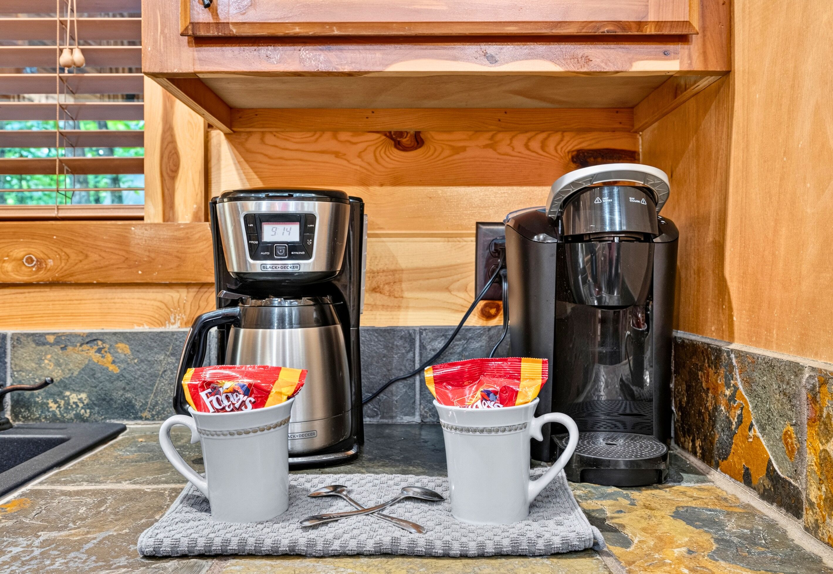 A kitchen area with a coffee maker, a kettle, and two mugs on a countertop.