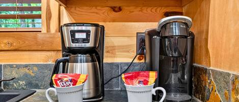 A kitchen area with a coffee maker, a kettle, and two mugs on a countertop.