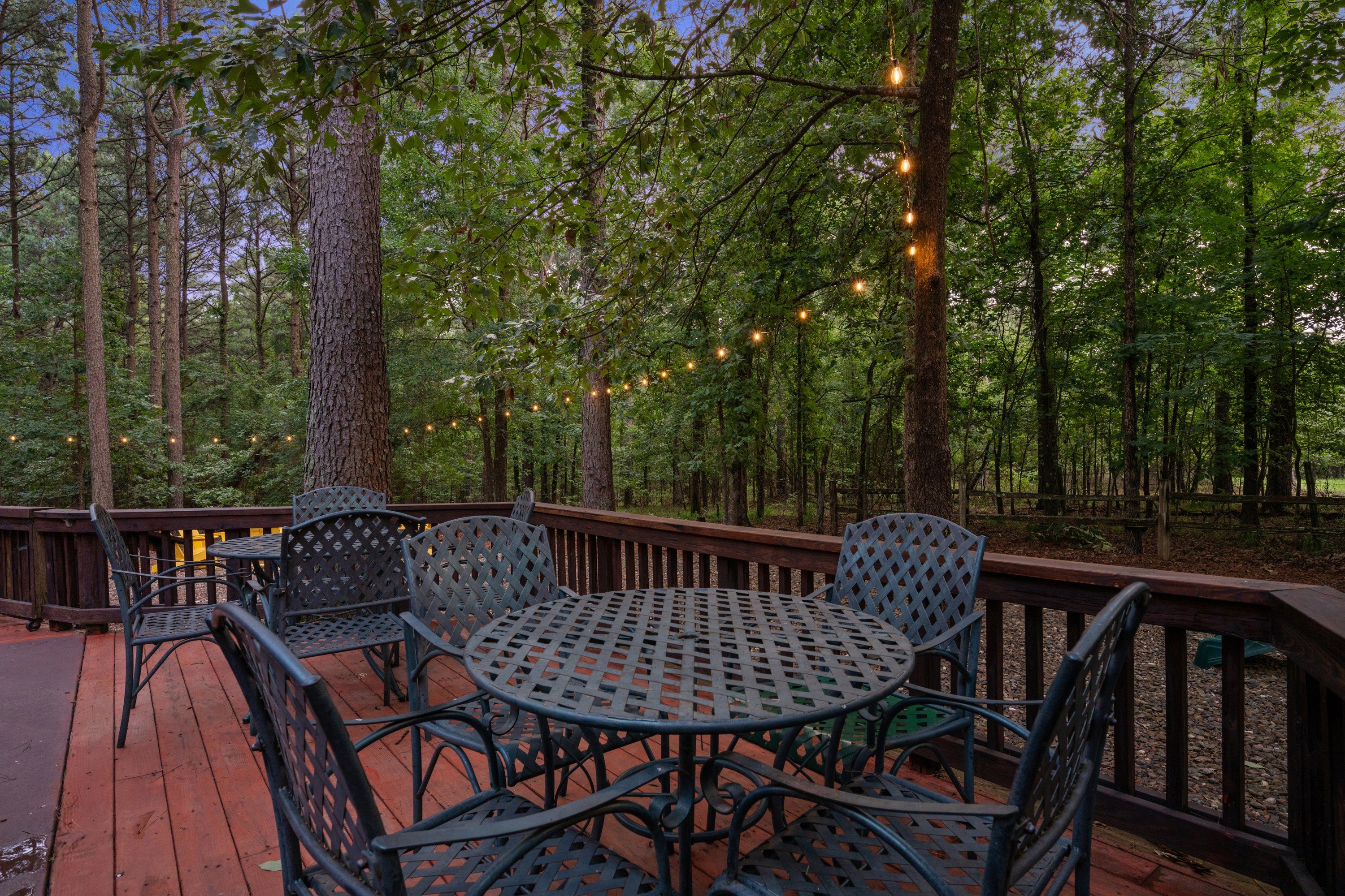 Eine Holzterrasse mit Metallstühlen und -tischen, umgeben von Bäumen und Lichterketten.