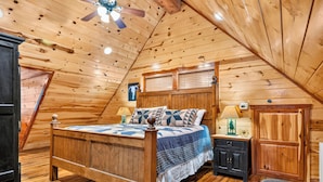 Un dormitorio con techo de madera, una cama con colcha, una mesita de noche, una lámpara y un armario.