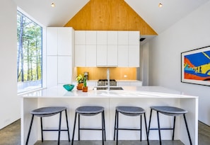 A modern kitchen with a central island, bar stools, and a large window. - Broken Bow Architectural Digest Featured Retreat (Broken Bow)