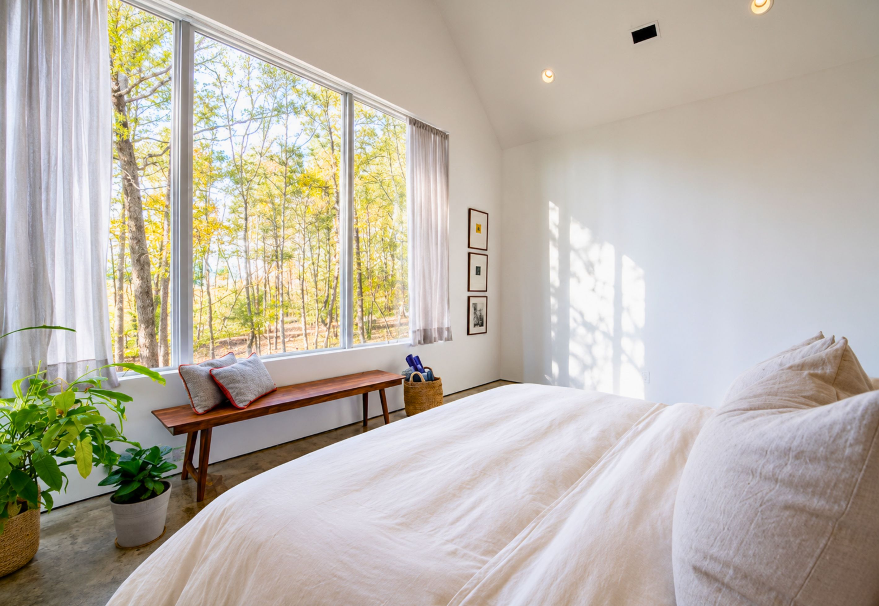 A bedroom with a large window, a bed, a bench, and a basket of items.
