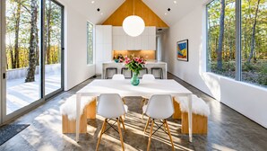 Een moderne keuken met een wit aanrecht, een hangende lamp en uitzicht op bomen door grote ramen.