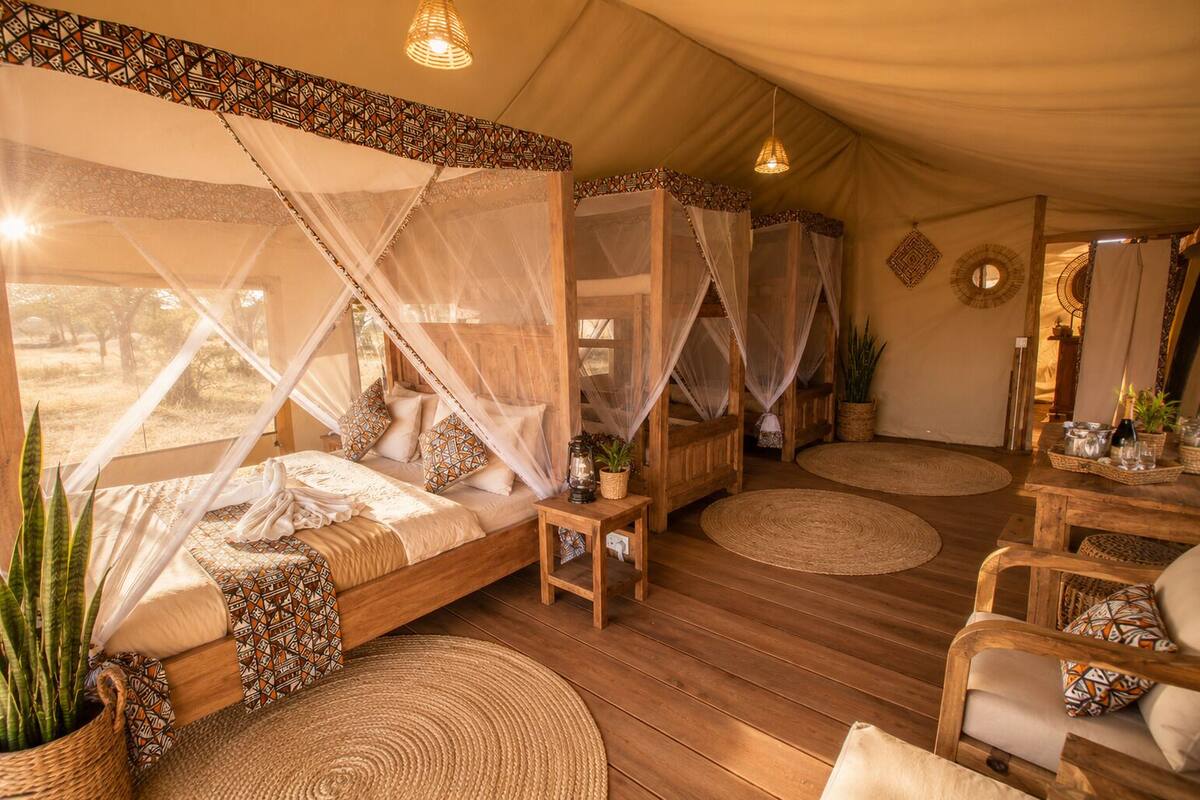 Une pièce aménagée sous une tente, avec un lit, deux chaises, une petite table et une vue sur l’extérieur.