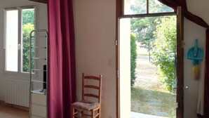 Een kamer met een houten plafond, een stoel, een radiator, een raam met gordijnen en een deur naar buiten.