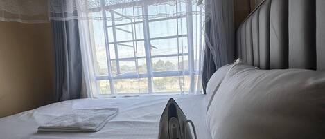 A hotel room with a bed, a window with curtains, and a wall-mounted iron.