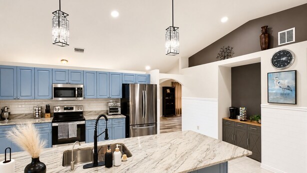 A modern kitchen with blue cabinets, stainless steel appliances, a marble island, pendant lighting, and a clock on the wall. - Pool Home/ Tropical Paradise Getaway Near Beaches and Downtown Fort Myers (Fort Myers)