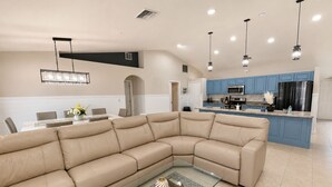 A modern kitchen with blue cabinets, a large island, and a beige sectional sofa. - Pool Home/ Tropical Paradise Getaway Near Beaches and Downtown Fort Myers (Fort Myers)