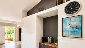 A hallway with a wooden floor, a black cabinet, a coffee maker, and a framed painting of a bird. - Pool Home/ Tropical Paradise Getaway Near Beaches and Downtown Fort Myers (Fort Myers)