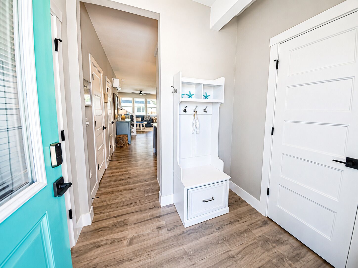 A hallway with wooden flooring, a teal door, and white doors with a coat rack.