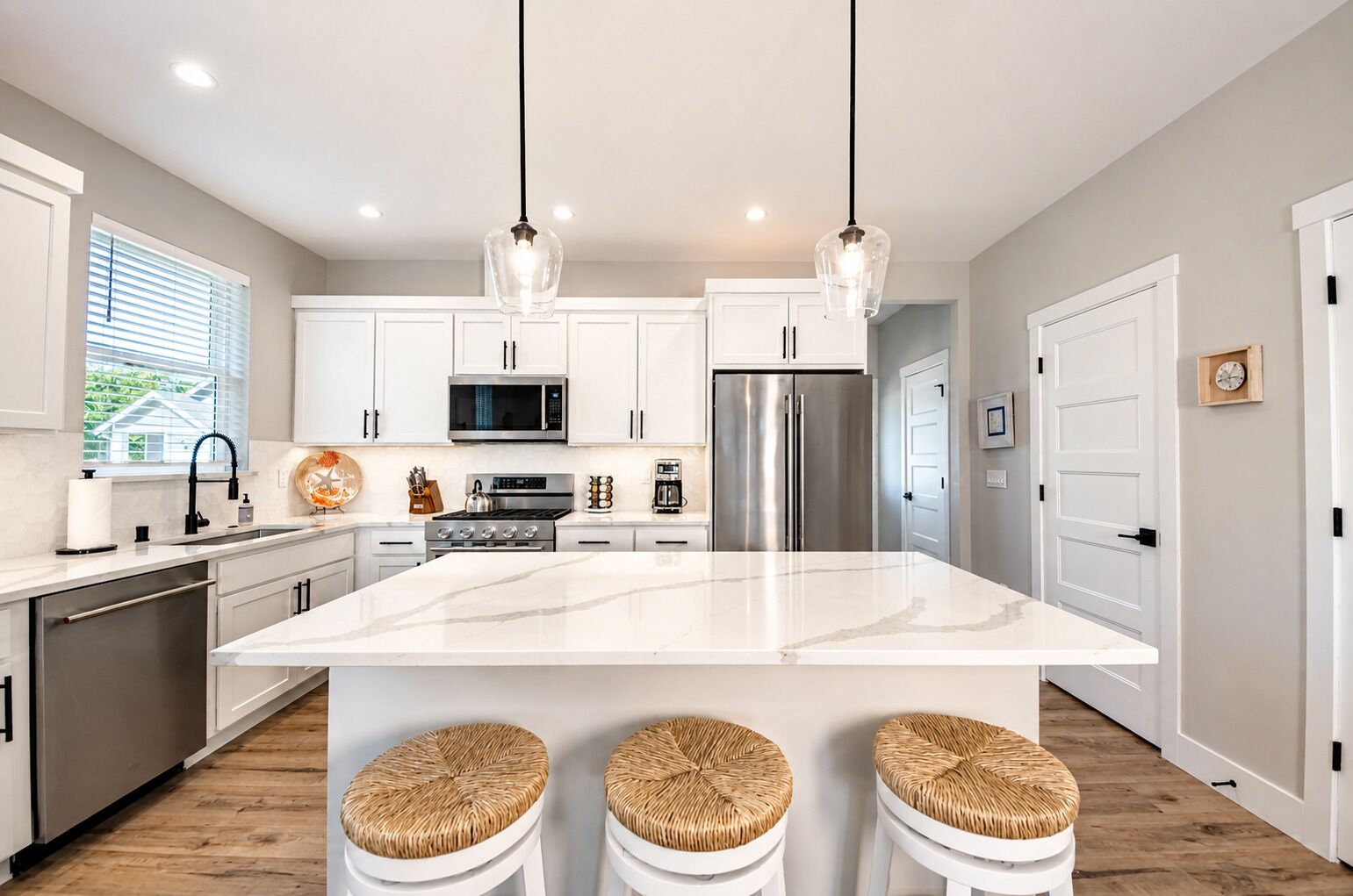 A modern kitchen with white cabinets, stainless steel appliances, a large island with stools, and pendant lighting.