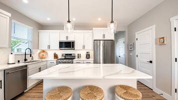 A modern kitchen with white cabinets, stainless steel appliances, a large island with stools, and pendant lighting.