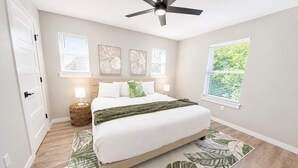 Ein Schlafzimmer mit einem Bett, einem Deckenventilator, einem Fenster mit Jalousien und Kunstwerken an der Wand.