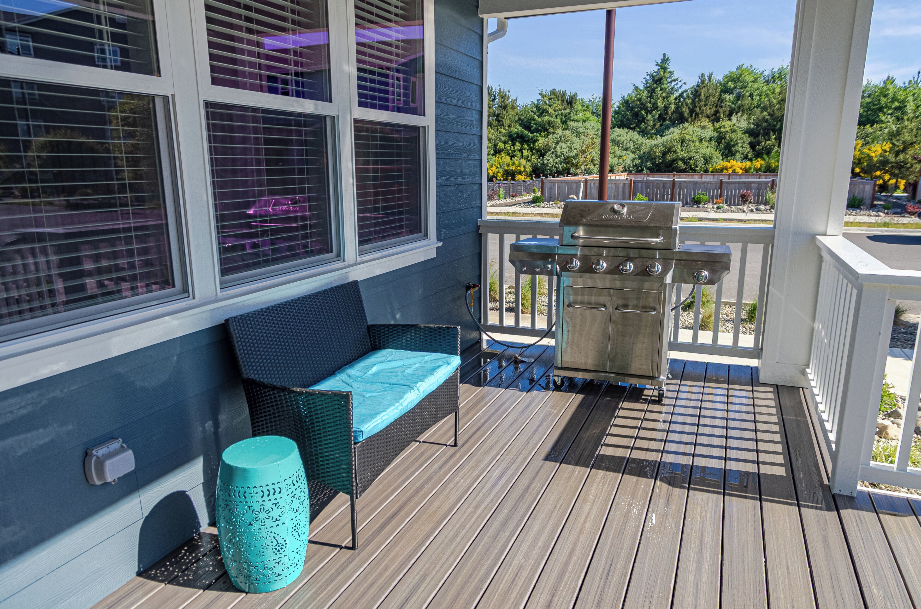 A covered porch with a grill, a cushioned seating area, and a view of the backyard.