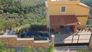 A yellow building with a red-tiled roof, a stone wall, and a parked car.