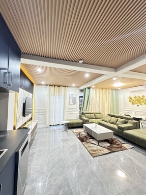 A modern living room with a sectional sofa, a coffee table, and a TV. - Spacious 2BR Retreat Luxury Living at Sapphire Suites (Accra)