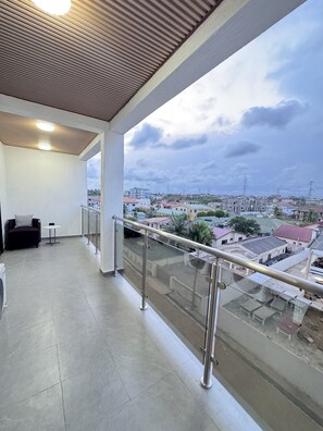 A balcony with a view of a residential area, a chair, and a small table. - Spacious 2BR Retreat Luxury Living at Sapphire Suites (Accra)