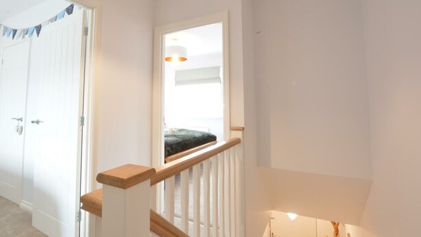 Eine Treppe mit hölzernem Geländer und weißen Spindeln, die zu einem Zwischenpodest mit einem Fenster und einem kleinen Tisch führt.