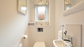 Ein kleines Badezimmer mit Toilette, Waschbecken, einem Fenster mit gemusterten Vorhängen und einem Spiegel.