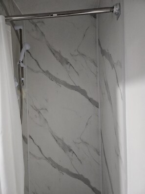 Un baño con pared de mármol, una barra para cortina de ducha y un cabezal de ducha.