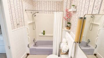 A bathroom with a bathtub, toilet, and sink, with floral wallpaper and a shower curtain.