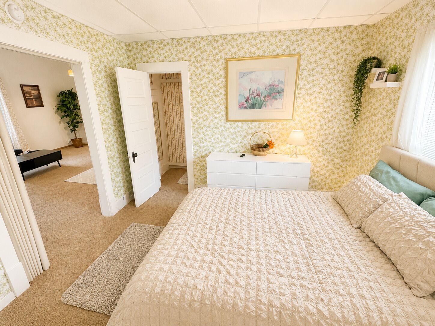 Ein Schlafzimmer mit Bett, Schminktisch, Nachttisch, Lampe und einem Gemälde an der Wand.