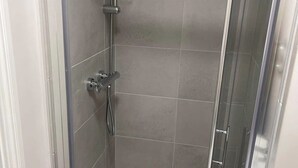 Um chuveiro com um chuveiro de mão, uma torneira embutida na parede e um box de vidro.