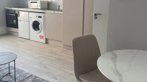 Uma cozinha compacta com máquina de lavar, micro-ondas e forno. Há uma mesa redonda com cadeiras e um tapete no chão.