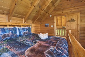 Ein Blockhaus-Zimmer mit einem Bett, das eine Bettdecke mit Rentier-Motiv, Holzwände und eine Holzbalkendecke aufweist.