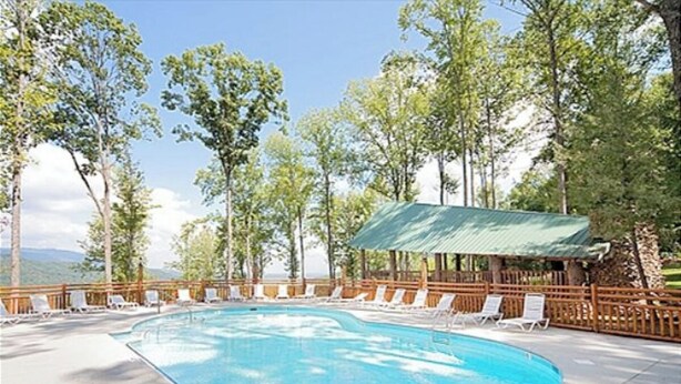 Una piscina con sillas de descanso, rodeada de árboles y una valla de madera.
