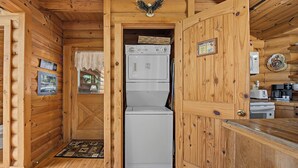 Interior de una cabaña de madera con zona de cocina, lavadora y refrigerador.