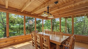 Un comedor de madera con una mesa grande y sillas, ventanas amplias y un ventilador de techo.