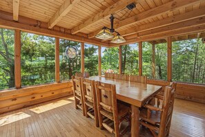 Ein Essbereich aus Holz mit einem großen Tisch, Stühlen, großen Fenstern und einem Deckenventilator.