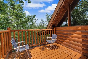 Eine Holzterrasse mit zwei Stühlen und einem Tisch, umgeben von Bäumen.
