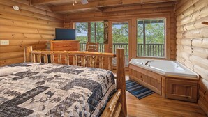 Un dormitorio tipo cabaña de madera con una cama, un televisor, un escritorio de madera, una silla, una ventana y un baño con bañera.