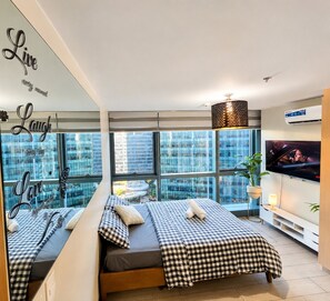 A modern hotel room with a large bed, a TV, a city view, and a mirror with motivational phrases. - Enjoy comfortable & spacious stay, perfectly located in the vibrant heart of BGC (Taguig)