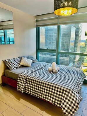 Ein Schlafzimmer mit großem Fenster, einem Bett mit karierter Bettwäsche und einer hängenden Leuchte.